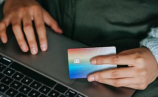 Close-Up von Person am Laptop mit Kreditkarte in der Hand